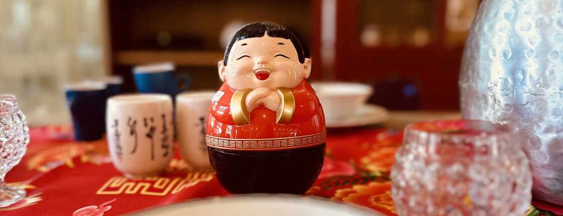 Eine freundliche asiatische Figur steht inmitten von exotischem Geschirr auf einem fein gedeckten Tisch im carla Store Bludenz.