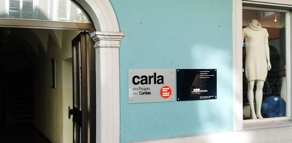 Außenansicht des carla-Shops in Feldkrich. Er befindet sich in einem alten, schönen, türkisfarbenen Gebäude. An der Außenfassade ist der Schriftzug "carla" angebracht. 