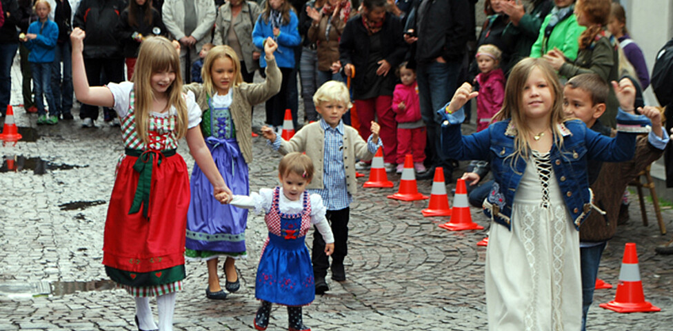 Kinder in Tracht laufen durch die feldkircher Innnenstadt. Sie sind dabei von Erwachsenen umbgeben, die zusehen. 