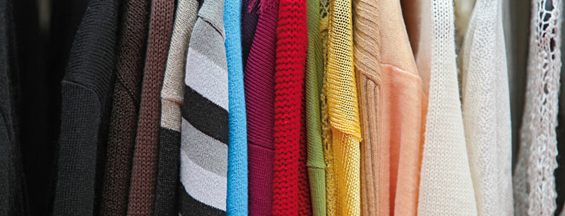 Nahaufnahme von Stoffpullovern unterschiedlicher Farben wie rot blau und gelb, die in einem Kleiderschrank hängen. 