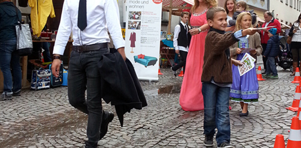 Sowohl ein junger Erwachsener als auch Kinder in Tracht gehen durch die feldkircher Innenstadt um ihre modische Kleidung zu präsentieren. 