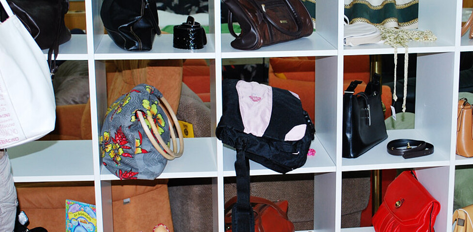 Handtaschen und Frauenschuhe stehen in einem quaderförmigen, weißen Regal. 