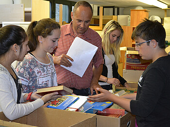 Lustenauer Schüler sind zu Gast bei der Carla. Sie wühlen in Kisten voller Bücher. Es sind drei Mädchen und ein Herr zu sehen.