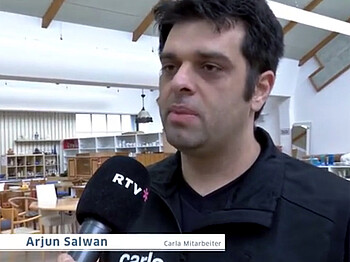 RTV im Interview mit carla-Mitarbeiter Arjun Salwan. Er trägt  kurze schwarze Haare und ebenfalls ein schwarzes Polo. 