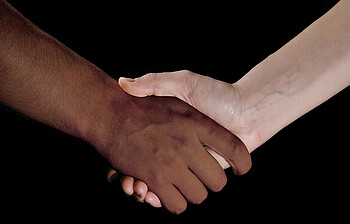 Zwei Menschen unterschiedlicher Ethnien geben sich gegenseitig ihre Hand. 
