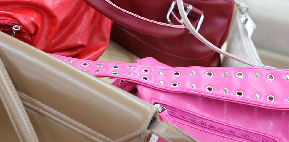 Eine rote, rosa und braune Handtasche liegen auf einer schlichten Unterlage. 